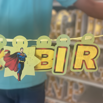 Close up detail of Superman Happy Birthday banner showing yellow letter tiles with Superman character illustrations