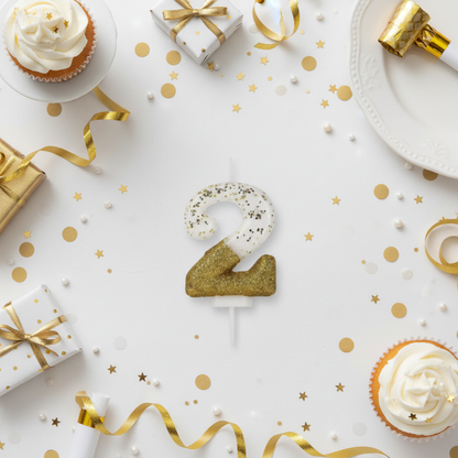 Semi glitter gold and white number 2 candle flat lay with gold ribbons gift boxes and party decor